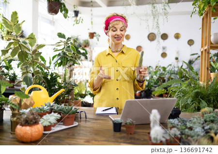 A woman in a yellow shirt is holding a cactus while teaching about plants in a bright, green environment A woman in a yellow shirt is holding a cactus while teaching about plants in a bright, green environment 136691742