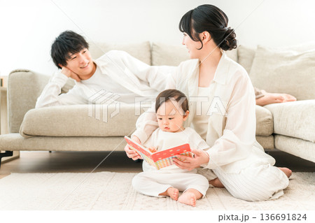 マイホームのリビングで子供,赤ちゃんに絵本を読む子育て世代のファミリー（育児,子育て,スキンシップ） 136691824