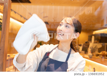エプロンを着てカフェの窓ガラスを拭く若い女性店員 エプロンを着てカフェの窓ガラスを拭く若い女性店員 136691952