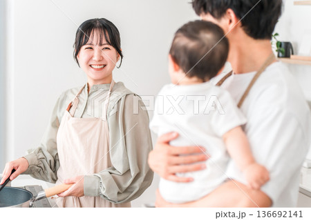 キッチンで赤ちゃんを抱っこするエプロン姿の夫婦,ファミリー 136692141