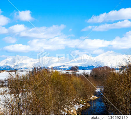 青空広がる冬の北海道美瑛町にある置杵牛川と十勝岳連峰の風景 136692189