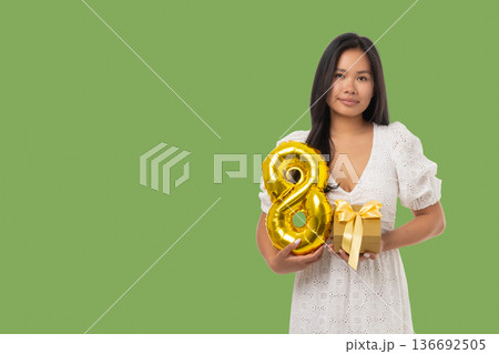 A young woman stands with a gold balloon number 8 and a gift 136692505