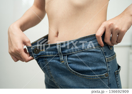 Young Asian woman losing weight wearing loose pants in oversize jeans. Young Asian woman losing weight wearing loose pants in oversize jeans. 136692909