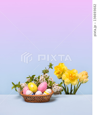 Multicolored Easter eggs in a basket with spring flowers: blooming spring cherry branches and yellow daffodils on gray table. Easter concept Multicolored Easter eggs in a basket with spring flowers: blooming spring cherry branches and yellow daffodils on gray table. Easter concept 136693682