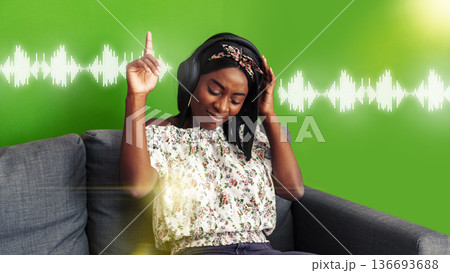 Listening to a podcast while sitting on a couch in front of a green background 136693688