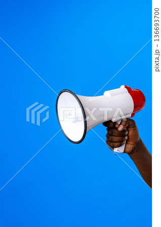 Loudspeaker held by hand against a bright blue background during a public speaking event Loudspeaker held by hand against a bright blue background during a public speaking event 136693700