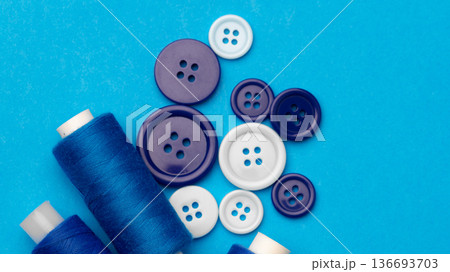 Sewing supplies arranged on a blue background with thread and buttons of different colors 136693703