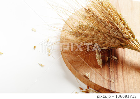 Harvested wheat on a wooden cutting board with scattered grains on a white surface Harvested wheat on a wooden cutting board with scattered grains on a white surface 136693715