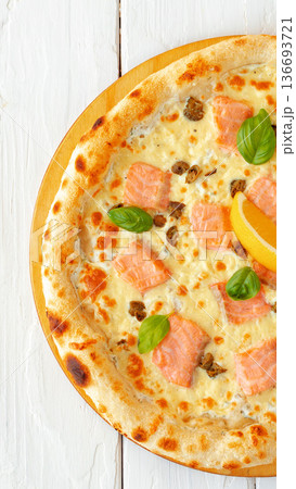 Fresh pizza with salmon, cheese, and basil on a wooden round board 136693721