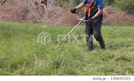 A man mows the grass with a trimmer on a summer day. A man mows the grass with a trimmer on a summer day. 136695503