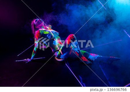 Sensual woman with fluorescent body paint posing in colorful smoke on dark background 136696766