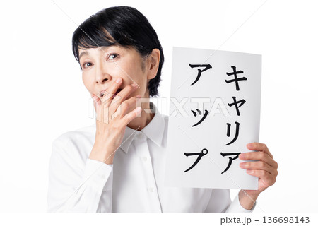 キャリアアップと書かれた紙を持ち口に手をあて嬉しそうなシニア女性 136698143
