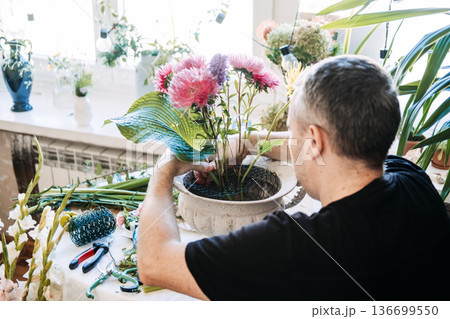 Man engaging in mindful floral arrangement at home. Floral meditation practice, slow arranging flowers, mindful floristry, zen flower therapy, meditative floral design. 136699550