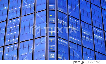 Big glowing windows in modern office building at night, in rows of windows light shines. Fragment of the glass facade of a modern corporate building at night. Modern glass office in city. Big glowing windows in modern office building at night, in rows of windows light shines. Fragment of the glass facade of a modern corporate building at night. Modern glass office in city. 136699739