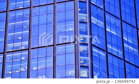 Big glowing windows in modern office building at night, in rows of windows light shines. Fragment of the glass facade of a modern corporate building at night. Modern glass office in city. Big glowing windows in modern office building at night, in rows of windows light shines. Fragment of the glass facade of a modern corporate building at night. Modern glass office in city. 136699742