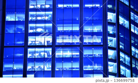Big glowing windows in modern office building at night, in rows of windows light shines. Fragment of the glass facade of a modern corporate building at night. Modern glass office in city. Big glowing windows in modern office building at night, in rows of windows light shines. Fragment of the glass facade of a modern corporate building at night. Modern glass office in city. 136699758