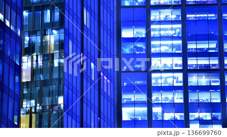 Big glowing windows in modern office building at night, in rows of windows light shines. Fragment of the glass facade of a modern corporate building at night. Modern glass office in city. Big glowing windows in modern office building at night, in rows of windows light shines. Fragment of the glass facade of a modern corporate building at night. Modern glass office in city. 136699760