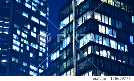 Big glowing windows in modern office building at night, in rows of windows light shines. Fragment of the glass facade of a modern corporate building at night. Modern glass office in city. Big glowing windows in modern office building at night, in rows of windows light shines. Fragment of the glass facade of a modern corporate building at night. Modern glass office in city. 136699777