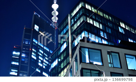Big glowing windows in modern office building at night, in rows of windows light shines. Fragment of the glass facade of a modern corporate building at night. Modern glass office in city. Big glowing windows in modern office building at night, in rows of windows light shines. Fragment of the glass facade of a modern corporate building at night. Modern glass office in city. 136699798