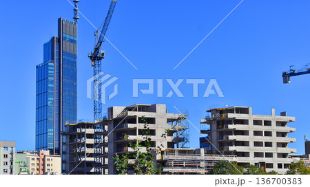 Crane on the construction site in a site surrounded by the high building. Apartment building under construction in the vicinity of high office building. Crane on the construction site in a site surrounded by the high building. Apartment building under construction in the vicinity of high office building. 136700383