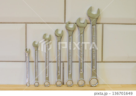 An organized set of chrome vanadium steel wrenches of various sizes, from small to large, arranged on a wooden workbench against a tiled wall.. High quality photo 136701649