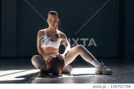 Sitting on the floor. Sportive woman is with basketball ball indoors Sitting on the floor. Sportive woman is with basketball ball indoors 136701796