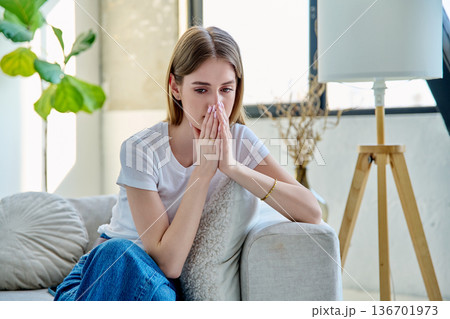 Sad unhappy stressed young woman sitting at home on sofa 136701973