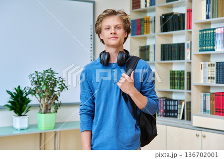 Portrait of smiling teenage student with backpack in classroom library 136702001