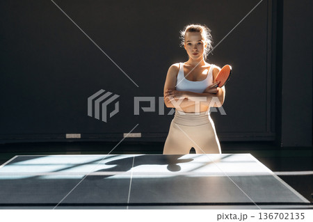 Front view, standing and posing. Beautiful young woman is by the tennis table indoors Front view, standing and posing. Beautiful young woman is by the tennis table indoors 136702135