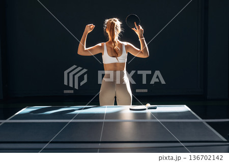 Ready to play, posing. Beautiful young woman is by the tennis table indoors Ready to play, posing. Beautiful young woman is by the tennis table indoors 136702142