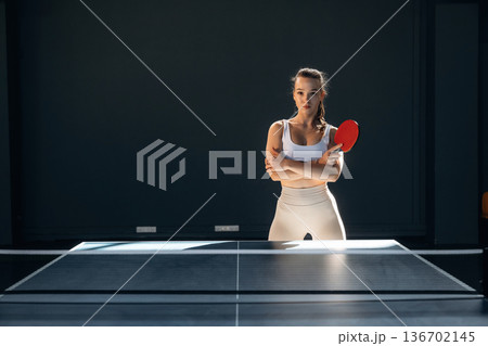 Ready to play, posing. Beautiful young woman is by the tennis table indoors Ready to play, posing. Beautiful young woman is by the tennis table indoors 136702145