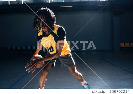 Wide motions by hands. Young black man is playing basketball indoors 136702234