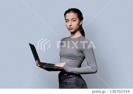 Portrait of serious teenage girl using laptop on gray background 136702544