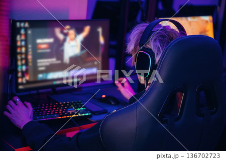 Gamer with white hair is sitting by computer indoors Gamer with white hair is sitting by computer indoors 136702723