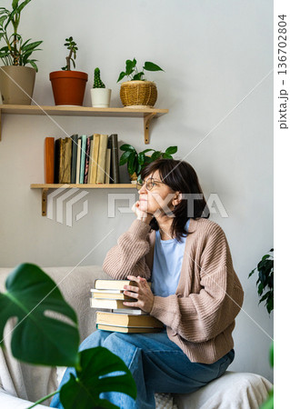 Mature woman daydreaming holding books at home 136702804