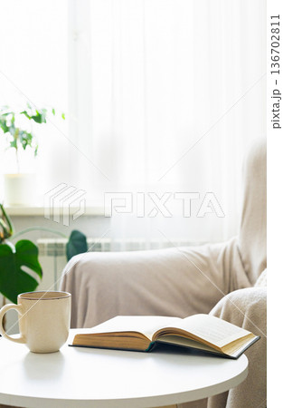 Warm bright living room scene with an open book and hot coffee on white table, creating relaxing comfortable atmosphere 136702811