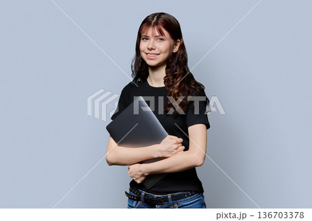 Portrait of beautiful girl teenage student holding laptop on gray background 136703378