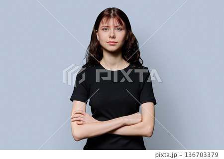 Portrait of smiling confident teenage girl with crossed arms on gray background 136703379