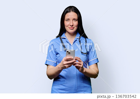 Portrait of smiling female nurse with smartphone, on white studio background Portrait of smiling female nurse with smartphone, on white studio background 136703542