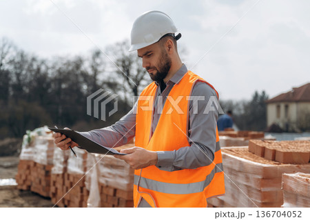 Holding notepad with documents. Construction worker is at job with bricks outdoors 136704052