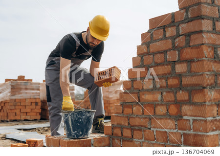 In uniform and hard hat. Construction worker is at job with bricks outdoors 136704069