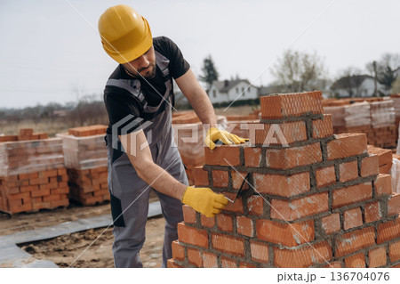 Foundation of wall. Construction worker is at job with bricks outdoors Foundation of wall. Construction worker is at job with bricks outdoors 136704076