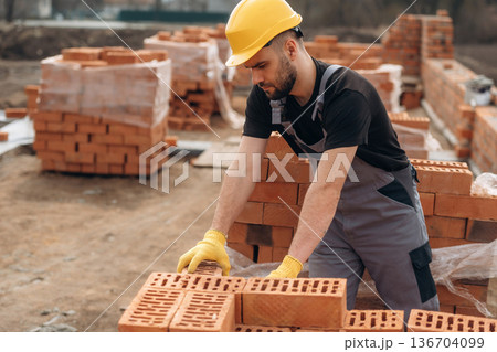 Busy by working with bricks. Construction worker is at job outdoors Busy by working with bricks. Construction worker is at job outdoors 136704099