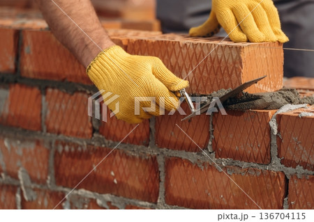 In yellow gloves. Close up view of construction man that is working with bricks 136704115