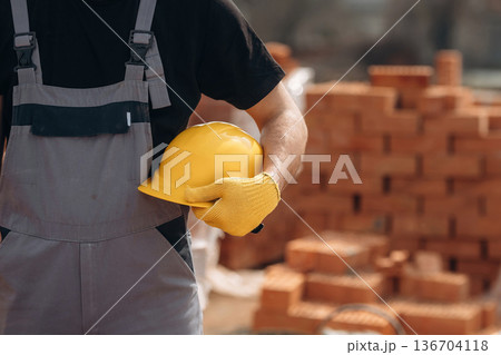 Holding hard hat. Close up view of construction man that is working with bricks Holding hard hat. Close up view of construction man that is working with bricks 136704118