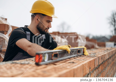 Using leveler tool. Construction worker is at job with bricks outdoors Using leveler tool. Construction worker is at job with bricks outdoors 136704136