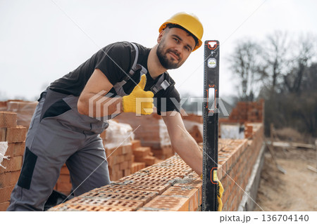Using leveler tool. Construction worker is at job with bricks outdoors 136704140