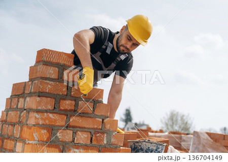 High up, placing bricks. Construction worker is at job outdoors High up, placing bricks. Construction worker is at job outdoors 136704149