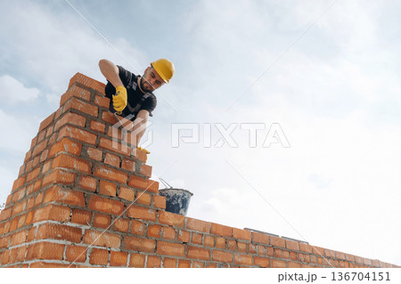 High up, placing bricks. Construction worker is at job outdoors 136704151