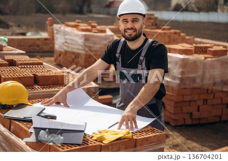 Positive facial expression, standing. Construction worker is at job with bricks outdoors 136704201